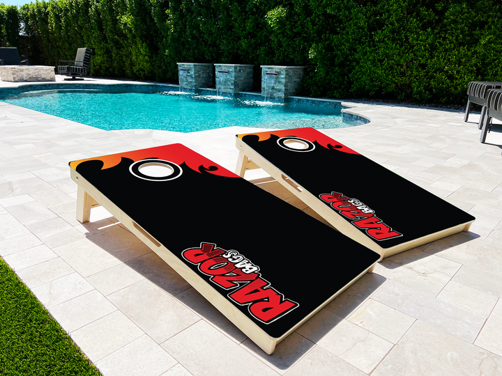 Two cornhole boards with a logo on a patio near a pool