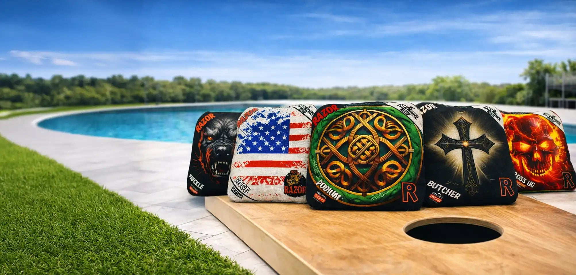 Cornhole boards with various designs on a grassy area near a pool