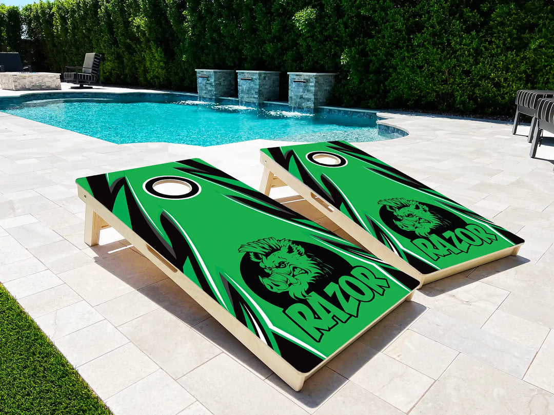 Two green cornhole boards with a logo and text on a patio near a pool.