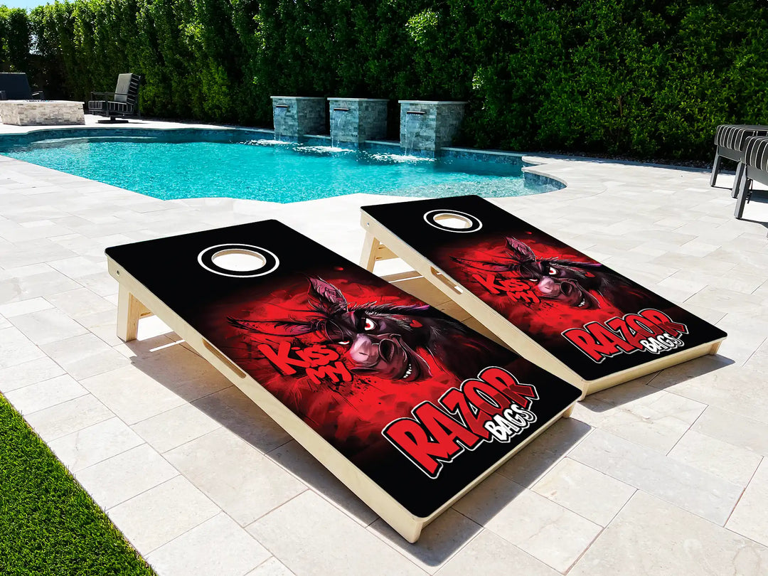 Two cornhole boards with a red and black design on a patio near a pool.