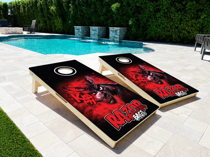 Two cornhole boards with a red and black design on a patio near a pool.