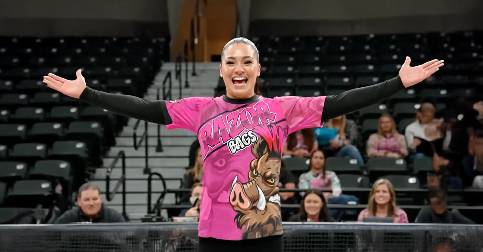 Person in a pink shirt with a graphic design, standing in an indoor arena with spectators.