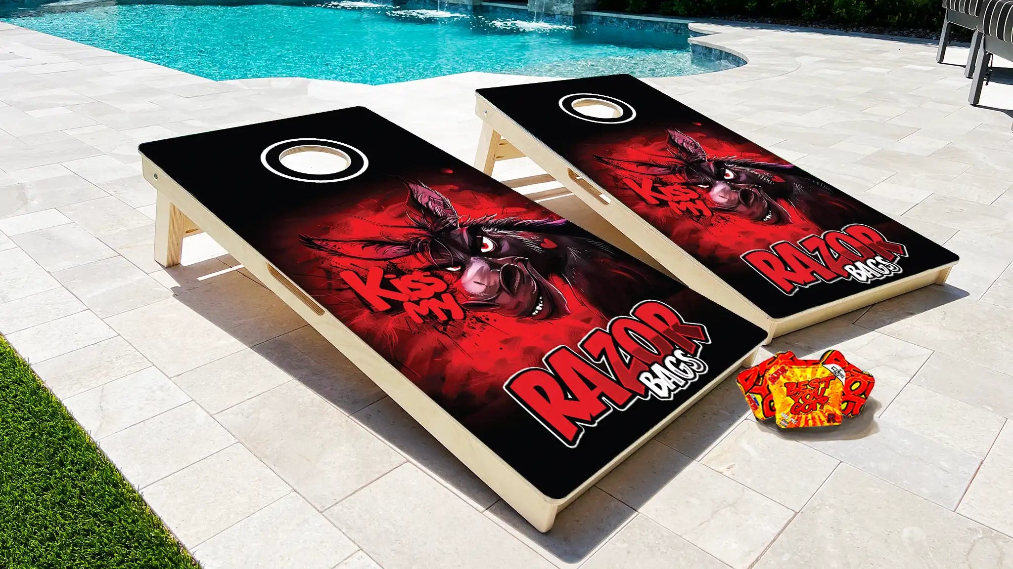 Two cornhole boards with a dog design and 'Razor' text on a patio near a pool.